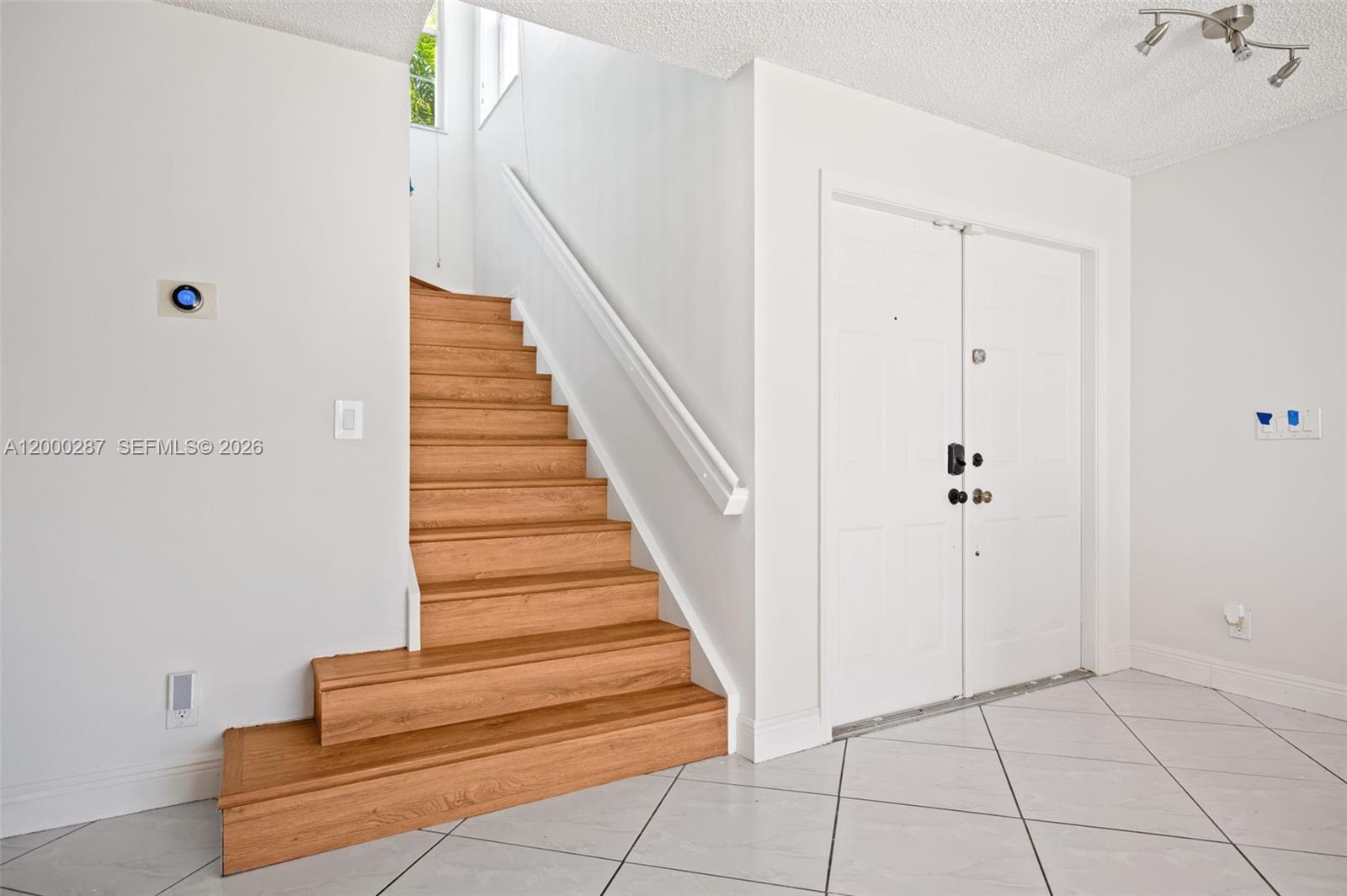 A wooden staircase with a white handrail sits next to double doors on tiled floors — 17357 SW 20th Ct, Miramar FL 33029, MIRAMAR, FL