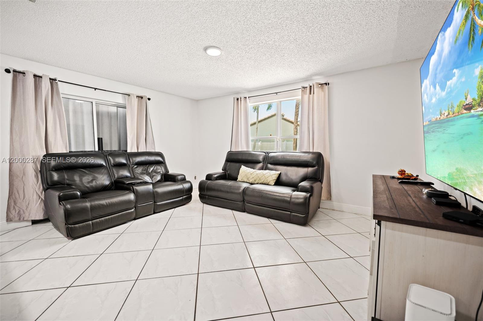 A living room features white tile floors, two black leather sofas, and a large television — 17357 SW 20th Ct, Miramar FL 33029, MIRAMAR, FL