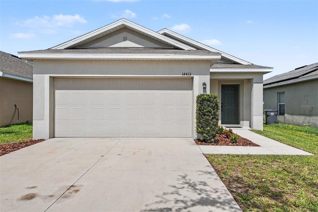 A single-story house features a beige stucco exterior, a two-car garage, and a front entryway — 14433 HADDON MIST DRIVE, WIMAUMA, FL