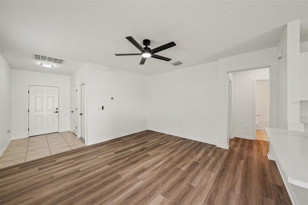 An interior view shows an open living area with wood-look flooring, a ceiling fan, and an entryway — 14433 HADDON MIST DRIVE, WIMAUMA, FL