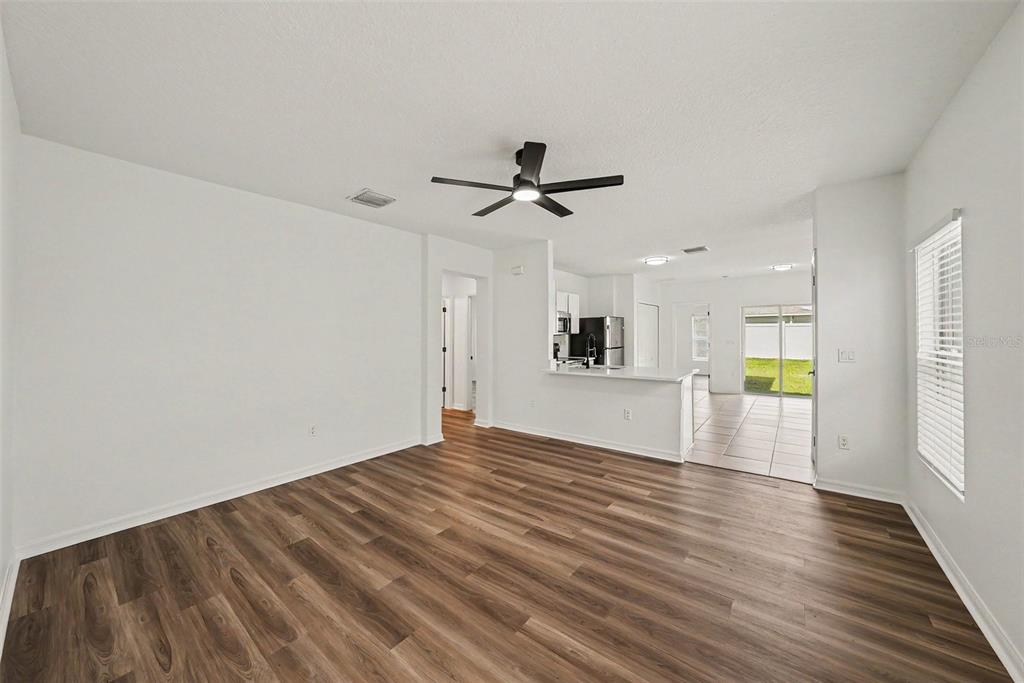 An open-concept living room with wood-look flooring, a ceiling fan, and an adjacent kitchen area — 14433 HADDON MIST DRIVE, WIMAUMA, FL