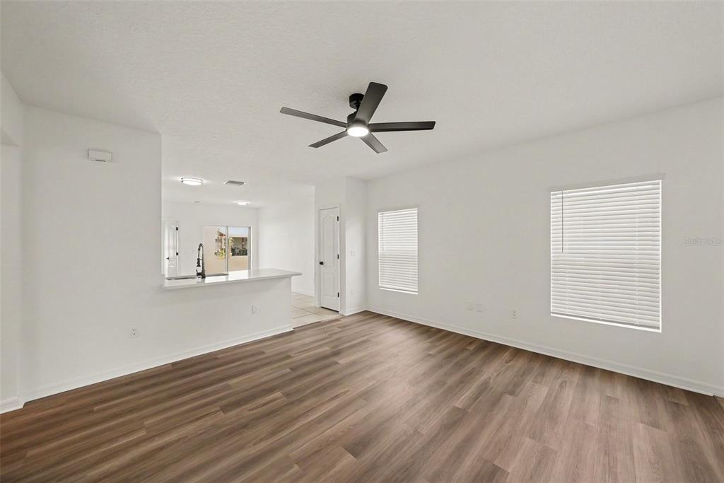 An open-concept living area features wood-look flooring, white walls, a ceiling fan, and a kitchen — 14433 HADDON MIST DRIVE, WIMAUMA, FL