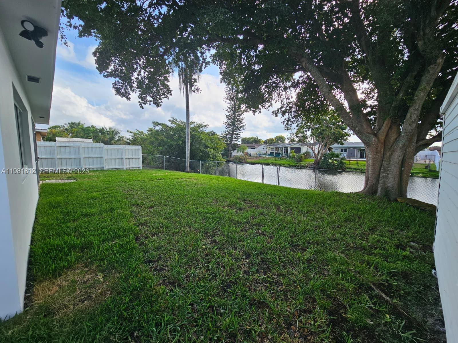 A grassy backyard features a large tree, a chain-link fence, and a canal view — 11450 NW 32nd Pl, Sunrise FL 33323, SUNRISE, FL