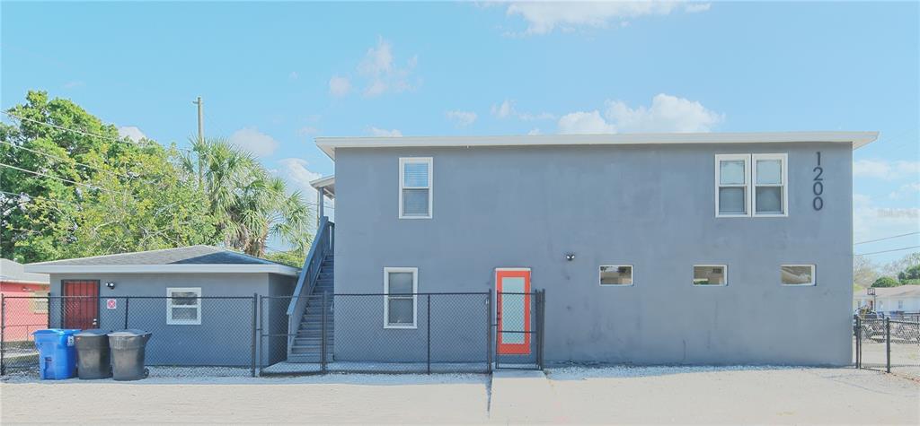 A two-story gray building with a fenced yard, exterior stairs, and a bright orange door — 1200 40TH STREET S, ST PETERSBURG, FL