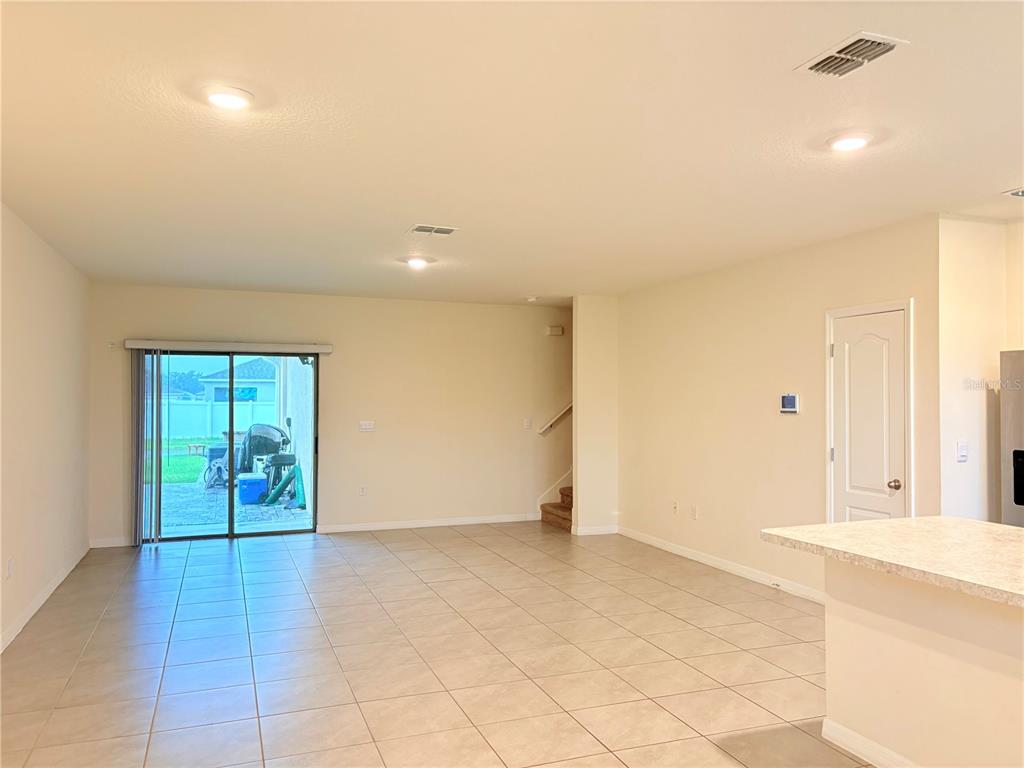 An open-concept living area features light tile flooring, recessed lighting, and a sliding glass door — 1559 CANDLEFIRE ROW, KISSIMMEE, FL