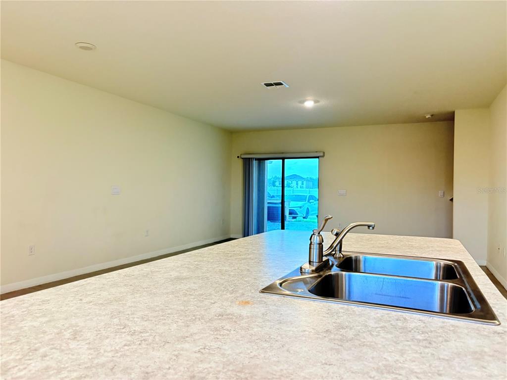 A kitchen island with a double-basin sink overlooks an open-concept living area with sliding doors — 1559 CANDLEFIRE ROW, KISSIMMEE, FL