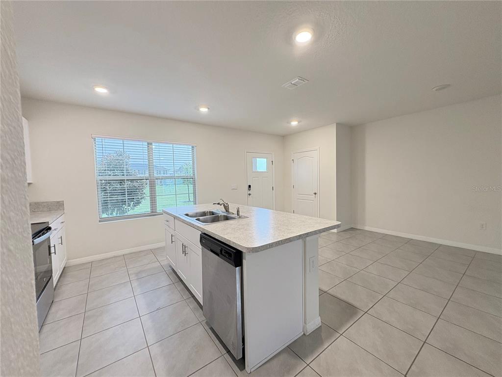 A kitchen features white cabinets, a central island with a sink, and light-colored tile flooring — 1559 CANDLEFIRE ROW, KISSIMMEE, FL