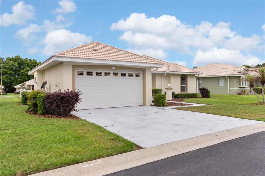 A single-story house with a white garage door, beige stucco walls, and a tiled roof — 117 HARBOR WAY, AUBURNDALE, FL