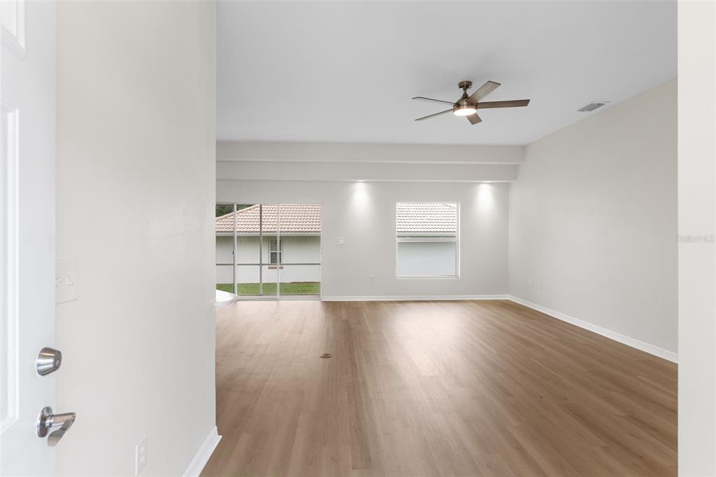 An empty living room features light wood-look flooring, a ceiling fan, and sliding glass doors — 117 HARBOR WAY, AUBURNDALE, FL