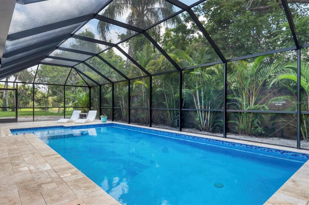 A screened-in swimming pool with a stone deck and lounge chairs surrounded by lush greenery — 2943 TUCKERSTOWN DRIVE, SARASOTA, FL
