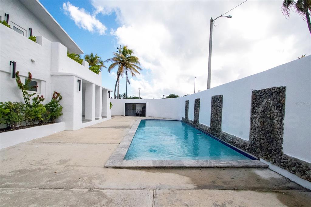 A rectangular swimming pool sits alongside a white building and a stone-accented wall — 2073 CACIQUE STREET, SAN JUAN, PR
