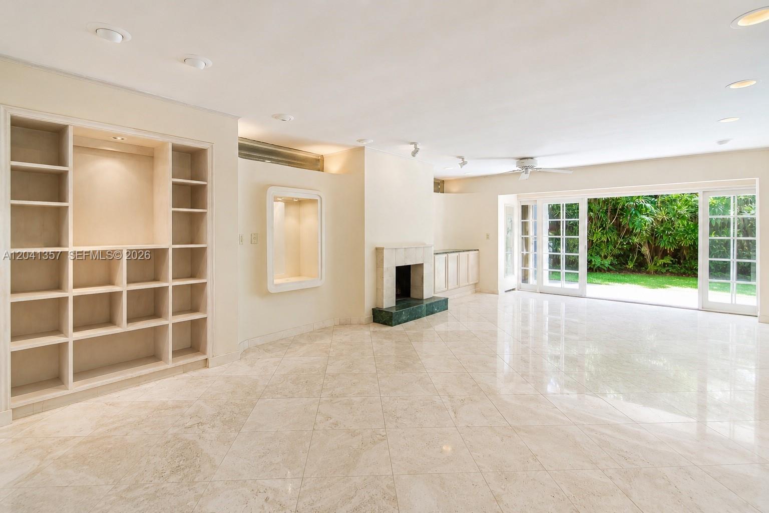 A bright living room features marble floors, built-in shelving, a fireplace, and sliding glass doors — 3441 Poinciana Ave, Miami FL 33133, MIAMI, FL