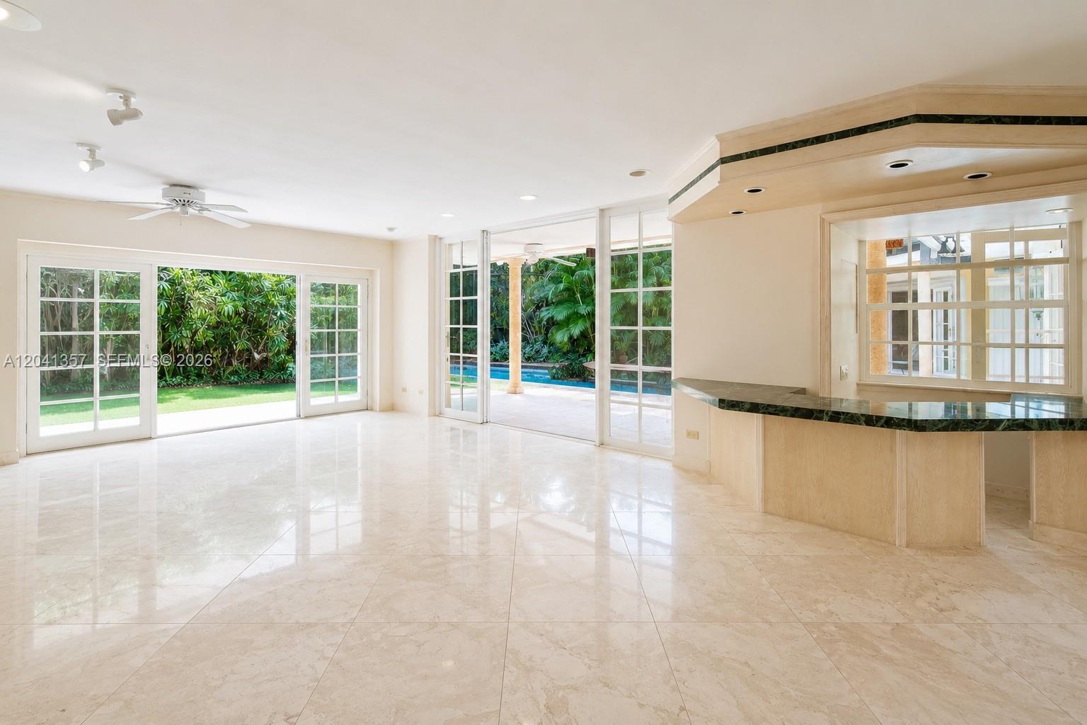 A spacious room features light tile flooring, a built-in bar, and sliding glass doors to a pool — 3441 Poinciana Ave, Miami FL 33133, MIAMI, FL