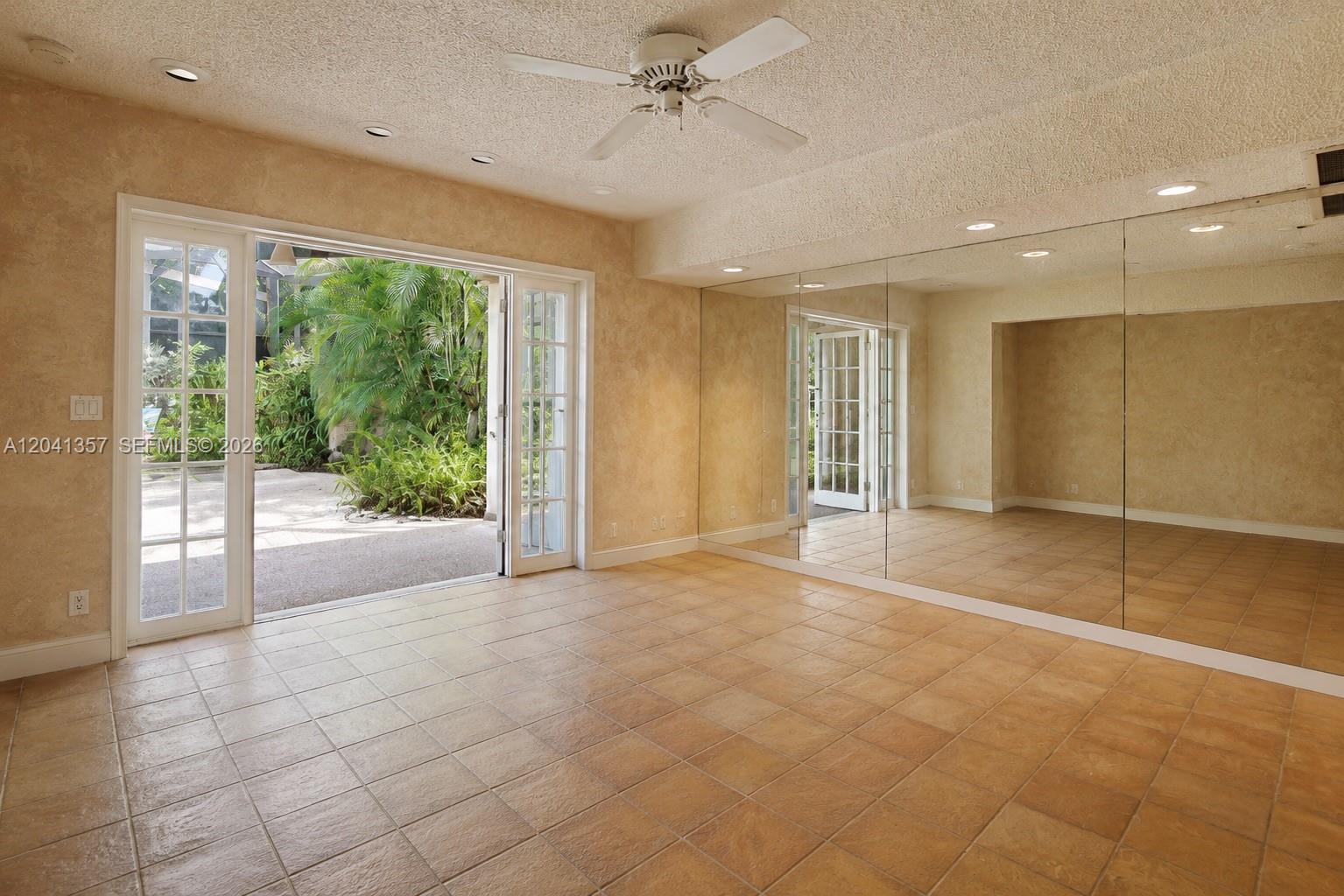 A room with tan tile flooring, mirrored walls, a ceiling fan, and glass doors to outdoors — 3441 Poinciana Ave, Miami FL 33133, MIAMI, FL