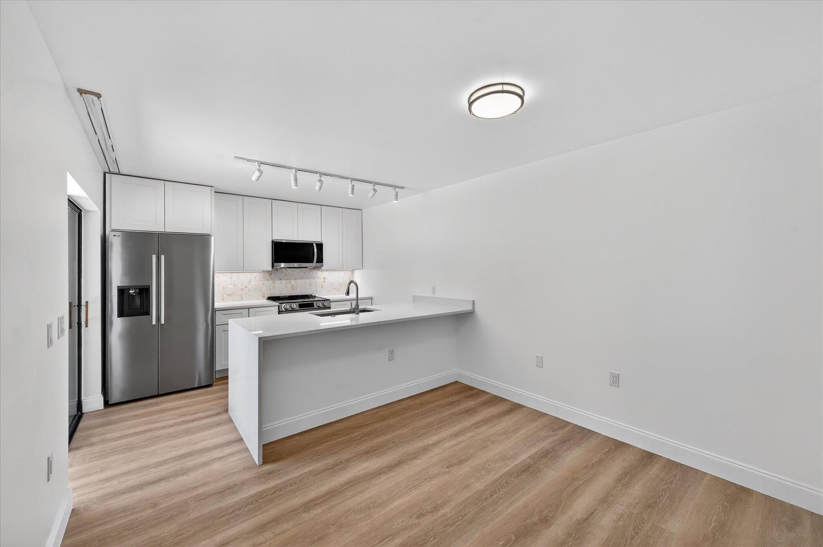 A modern kitchen features white cabinetry, stainless steel appliances, and a peninsula with quartz countertops — 1617 16th Way, West Palm Beach FL 33407, WEST PALM BEACH, FL