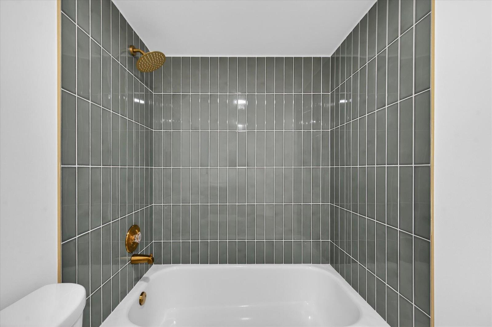 A bathroom shower area features vertical grey subway tiles, a white tub, and gold fixtures — 1617 16th Way, West Palm Beach FL 33407, WEST PALM BEACH, FL