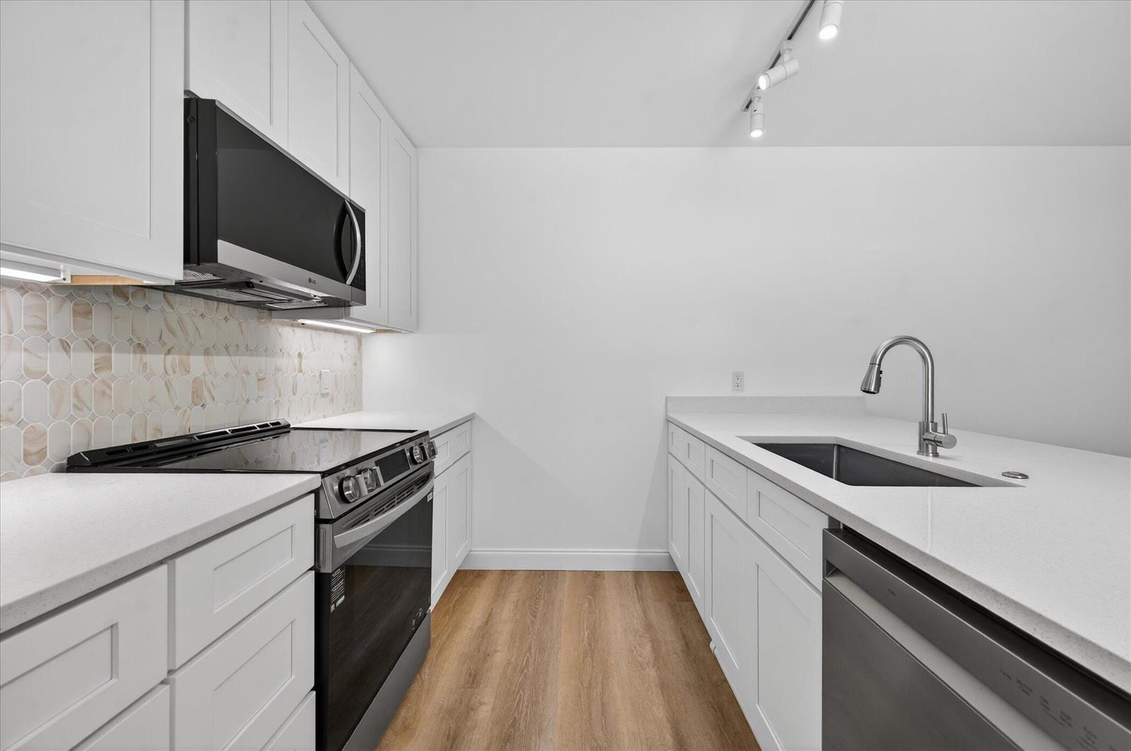 A modern kitchen features white cabinetry, stainless steel appliances, quartz countertops, and a tile backsplash — 1617 16th Way, West Palm Beach FL 33407, WEST PALM BEACH, FL