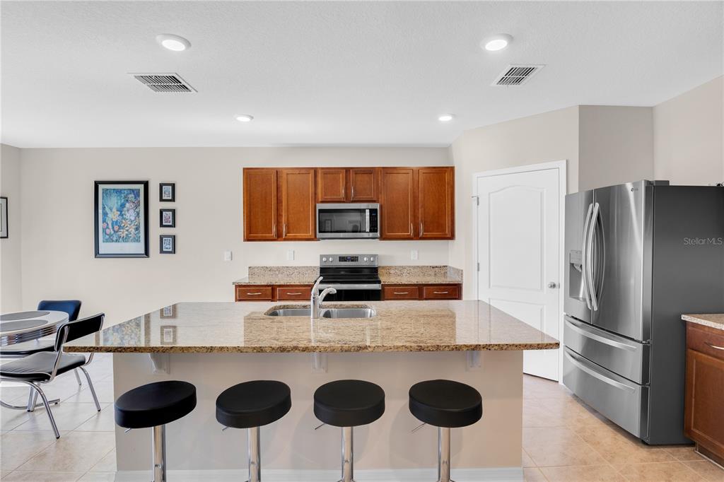 A kitchen features a granite-topped island with bar stools, wooden cabinets, and stainless steel appliances — 204 INMAN BOULEVARD, WINTER HAVEN, FL