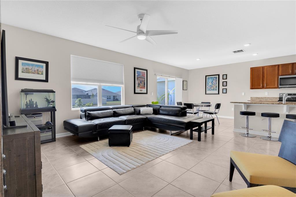 An open-concept living room features a black sectional sofa, tile flooring, and an adjacent kitchen — 204 INMAN BOULEVARD, WINTER HAVEN, FL