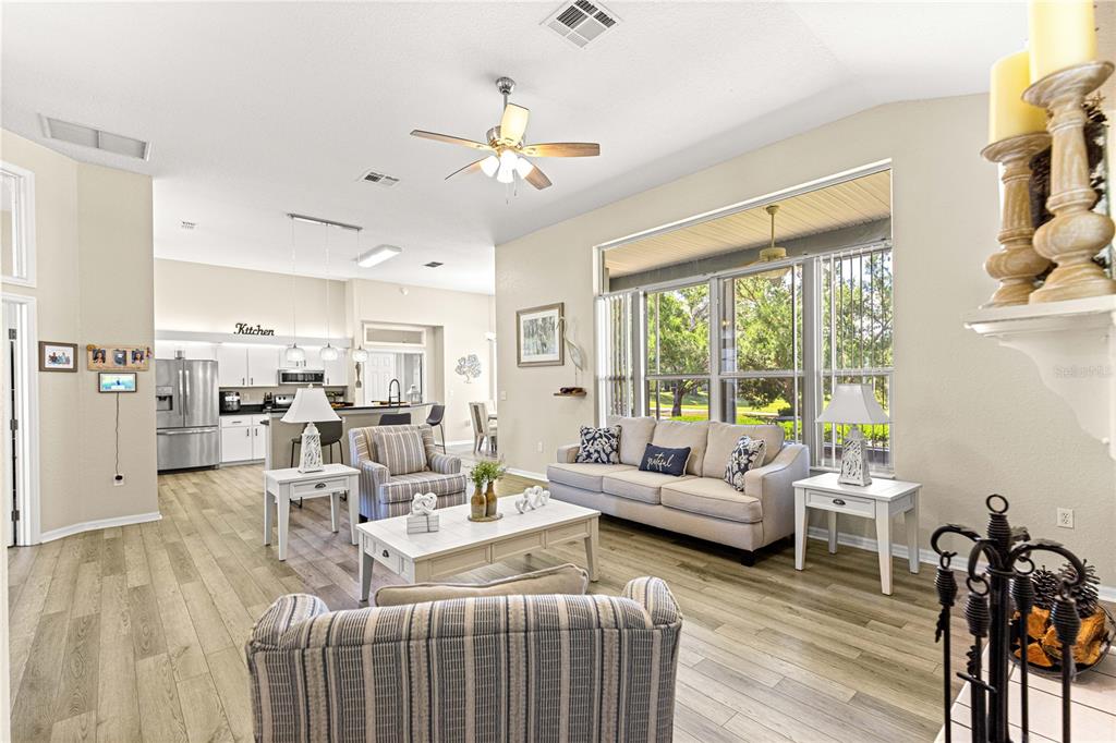 A living room with light wood flooring, a beige sofa, and an open-concept kitchen — 6744 SW 113TH PLACE, OCALA, FL
