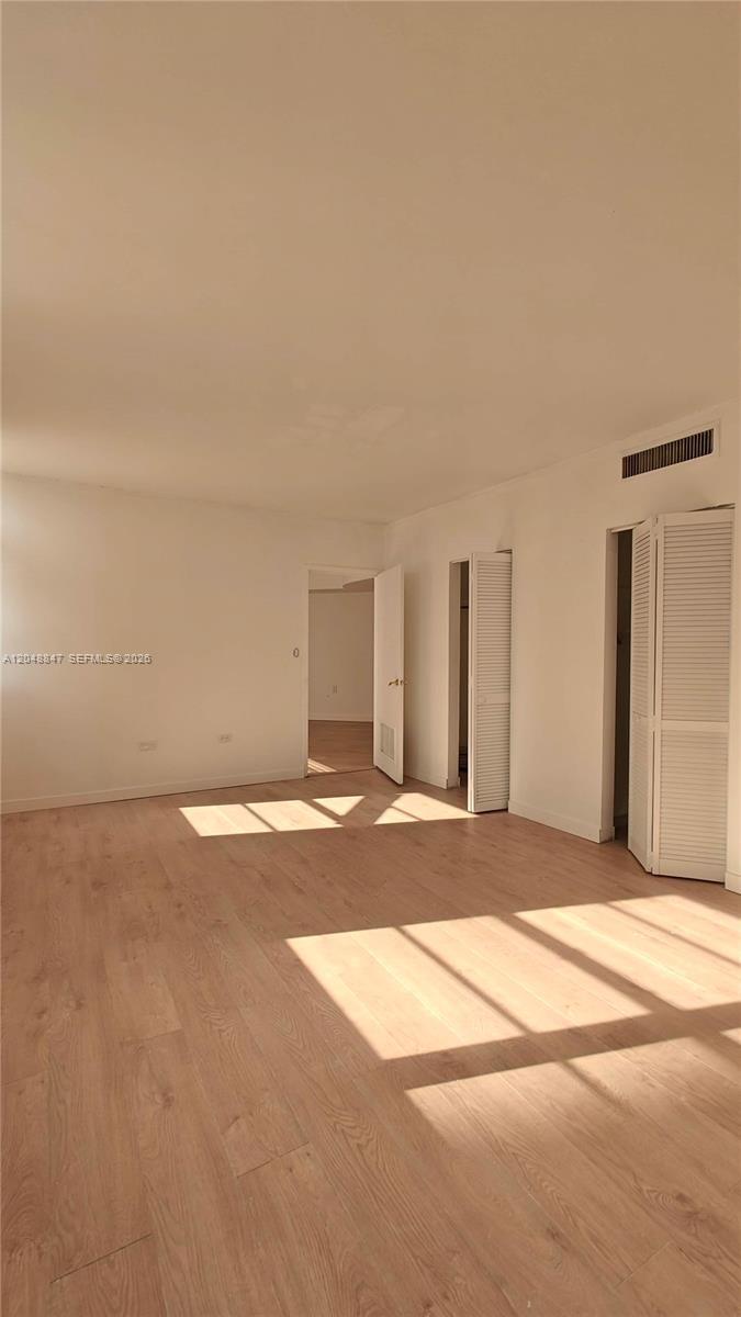 An empty room features light wood-look flooring, white walls, and two sets of louvered closet doors — 801 Brickell Bay Dr # 365, Miami FL 33131, MIAMI, FL