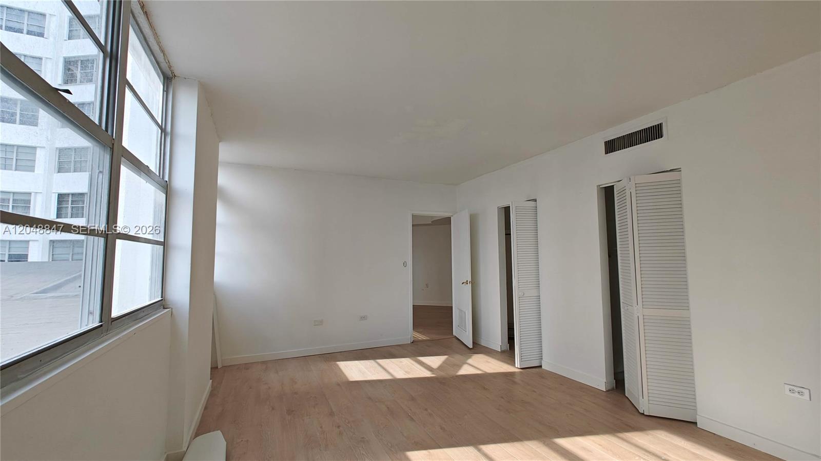 An empty room features white walls, light wood-look flooring, louvered closet doors, and large windows — 801 Brickell Bay Dr # 365, Miami FL 33131, MIAMI, FL