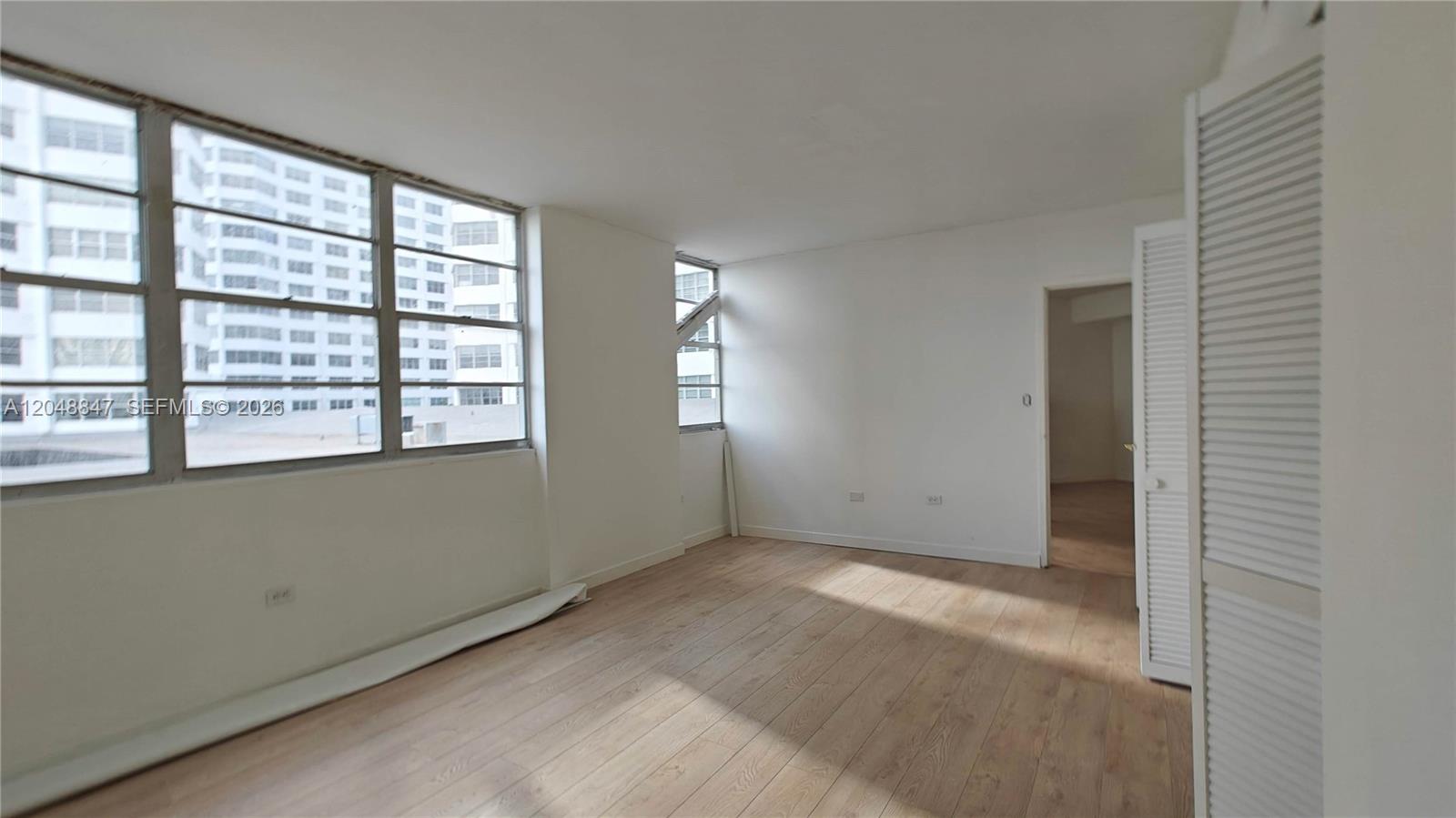 An empty room features light wood-look flooring, white walls, and large windows overlooking city buildings — 801 Brickell Bay Dr # 365, Miami FL 33131, MIAMI, FL