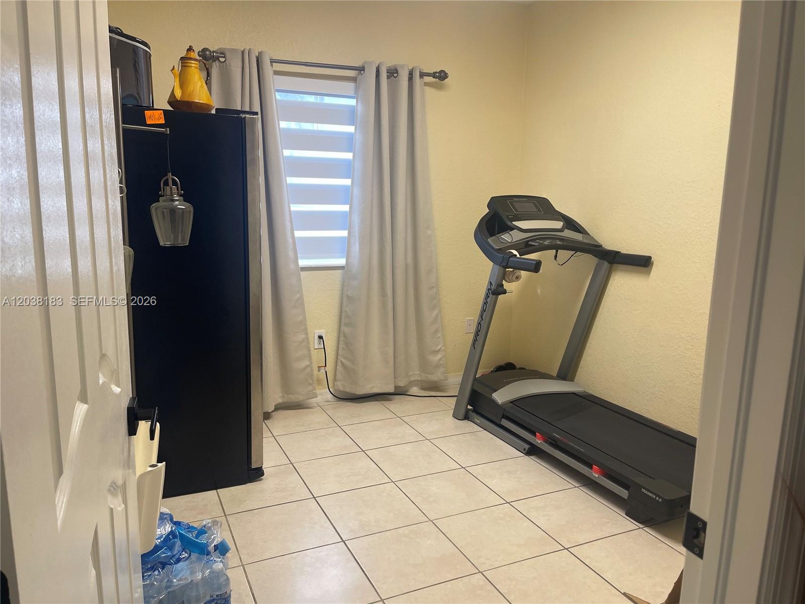 A small room with tiled floors contains a treadmill and a black refrigerator — 16364 SW 44th Way, Miami FL 33185, MIAMI, FL