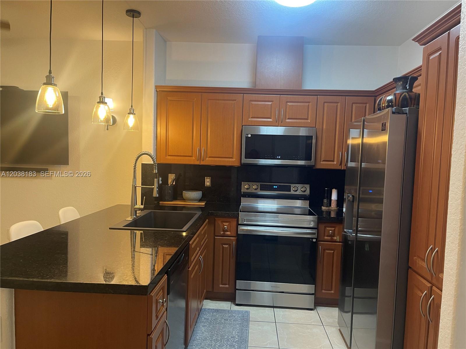 A kitchen features wood cabinets, black countertops, stainless steel appliances, and three hanging pendant lights — 16364 SW 44th Way, Miami FL 33185, MIAMI, FL