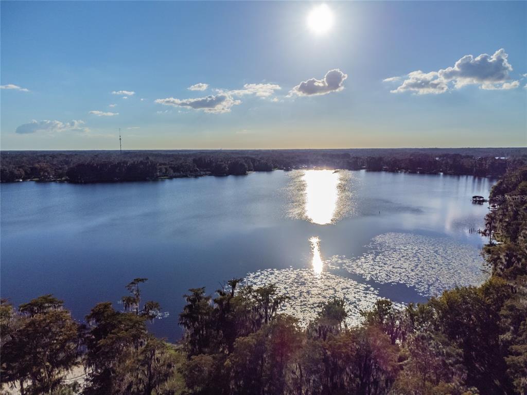 An aerial view of a lake surrounded by trees with sunlight reflecting on the water — DAVISTA, NEW PORT RICHEY, FL