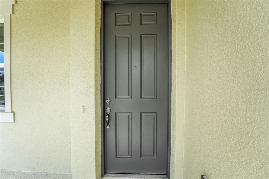 A gray six-panel front door is set into a light yellow stucco exterior wall — 5213 WAYPOINTE BOULEVARD, APOPKA, FL