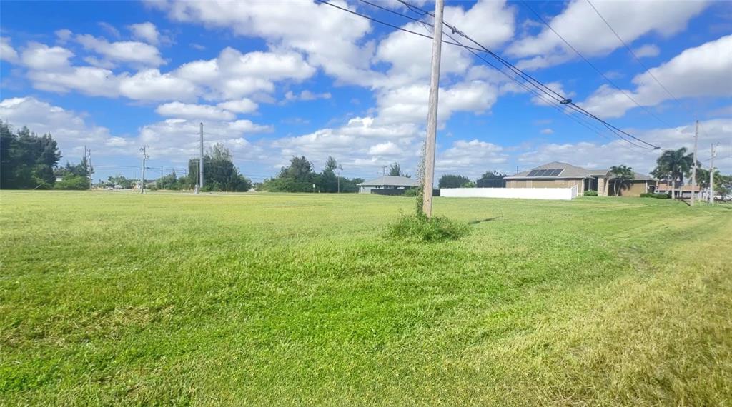 A large, grassy vacant lot features a utility pole and nearby residential houses — 312 SW 15TH STREET, CAPE CORAL, FL
