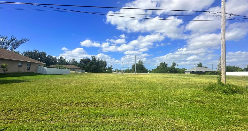 A wide, grassy vacant lot is situated between two residential houses under a blue sky — 312 SW 15TH STREET, CAPE CORAL, FL
