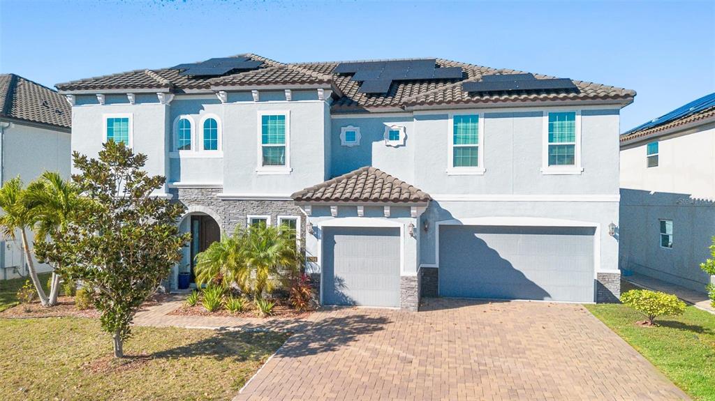 A two-story house with a light blue exterior, stone accents, solar panels, and a paved driveway — 8324 LUDINGTON CIRCLE, ORLANDO, FL