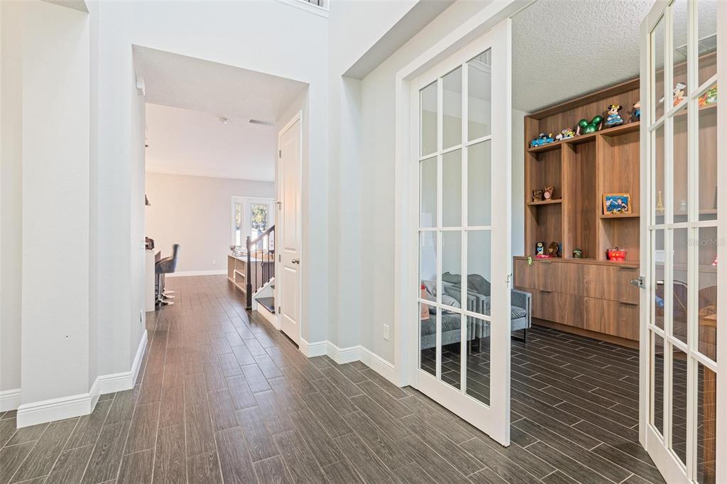 A hallway with wood-look tile flooring leads to a room with French doors and shelving — 8324 LUDINGTON CIRCLE, ORLANDO, FL