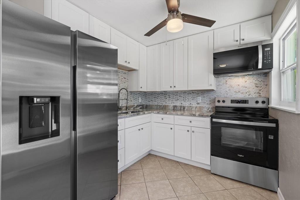 A kitchen features white cabinets, stainless steel appliances, a patterned backsplash, and tile flooring — 6024 MERRIL STREET, NORTH PORT, FL