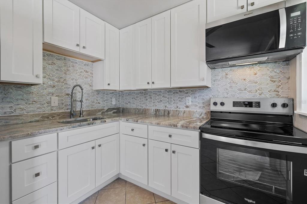 A kitchen features white cabinets, a stone countertop, a tiled backsplash, and stainless steel appliances — 6024 MERRIL STREET, NORTH PORT, FL