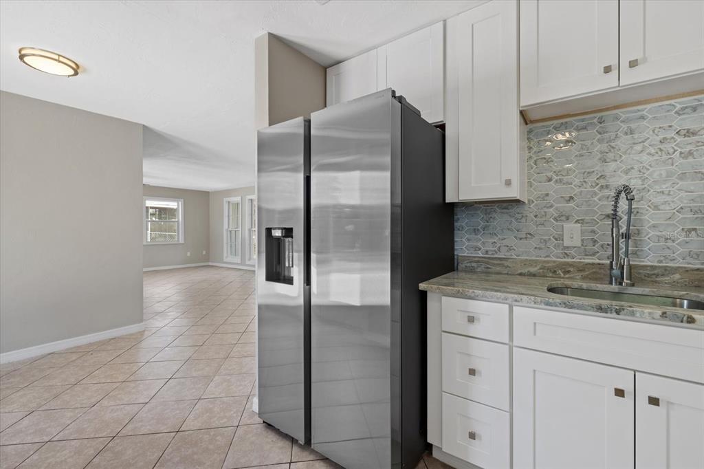 A kitchen features white cabinets, a stainless steel refrigerator, and a patterned tile backsplash — 6024 MERRIL STREET, NORTH PORT, FL