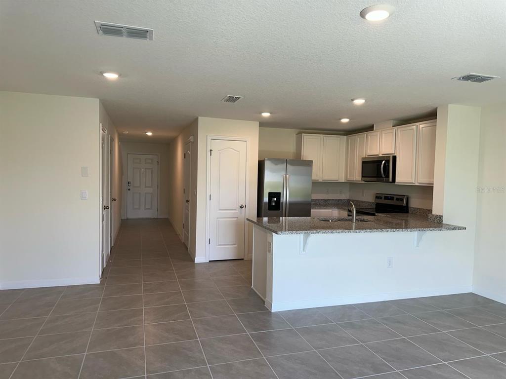 A kitchen with white cabinets and granite countertops overlooks a tiled living area — 2923 BRIE HAMMOCK BEND, ST CLOUD, FL
