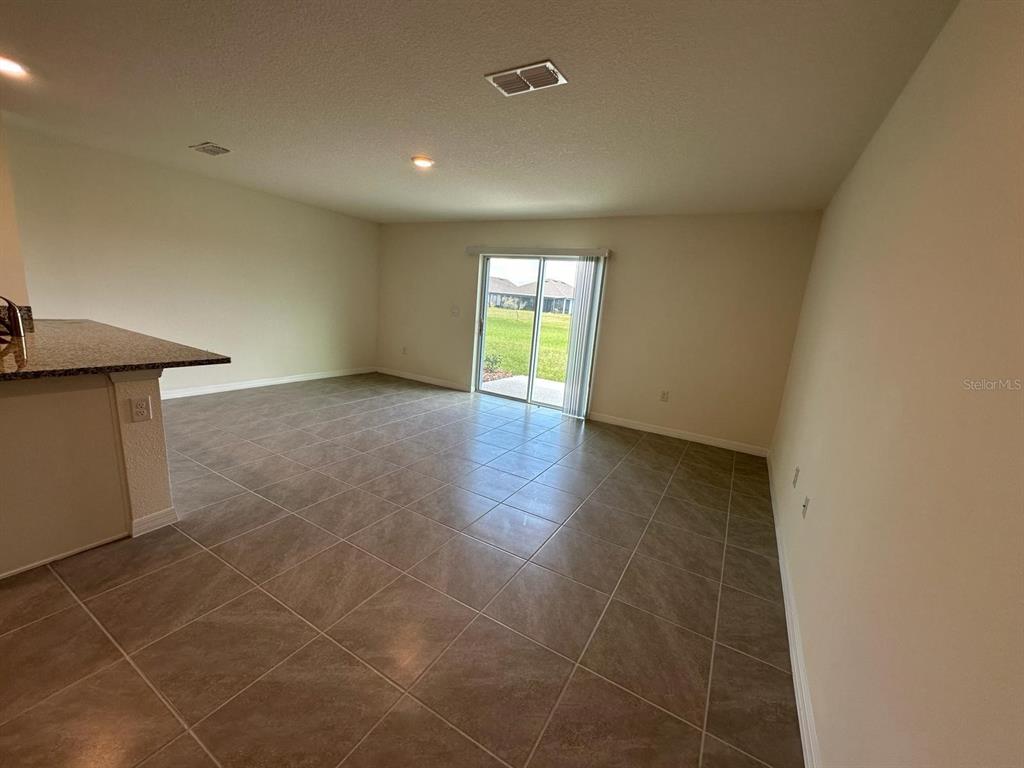 An open-concept living area features light-colored tile flooring, a granite-topped counter, and sliding glass doors — 2923 BRIE HAMMOCK BEND, ST CLOUD, FL