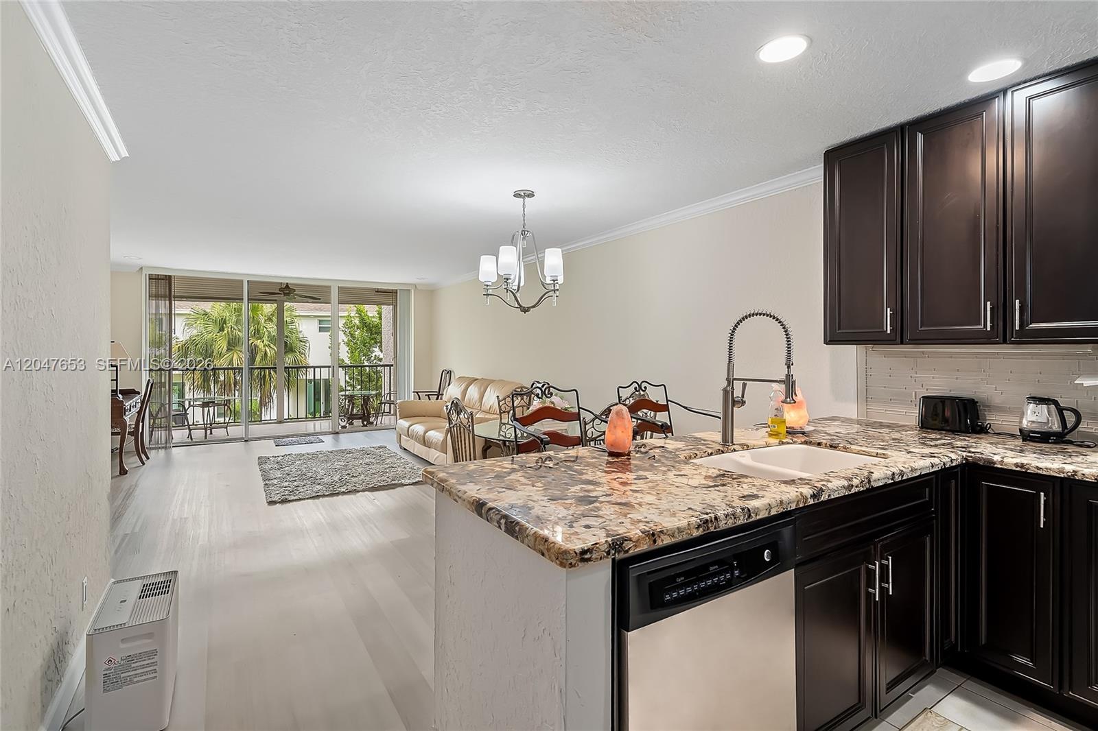 A kitchen with dark cabinets and granite countertops overlooks an open-concept living and dining area — 4345 Trevi Ct # 202, Lake Worth FL 33467, LAKE WORTH, FL