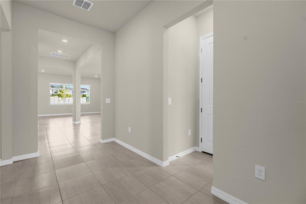 A hallway with light-colored tile flooring leads toward an open living area with windows — 10411 PARK ESTATES AVENUE, ORLANDO, FL