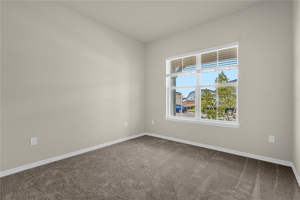 An empty bedroom with beige walls, gray carpet, and a window overlooking a neighborhood — 10411 PARK ESTATES AVENUE, ORLANDO, FL