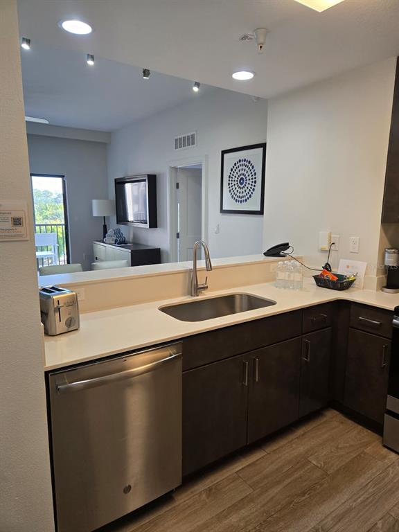 A kitchen features a stainless steel dishwasher, dark cabinetry, and a sink overlooking a living area — 14501 GROVE RESORT AVENUE UNIT 3424, WINTER GARDEN, FL