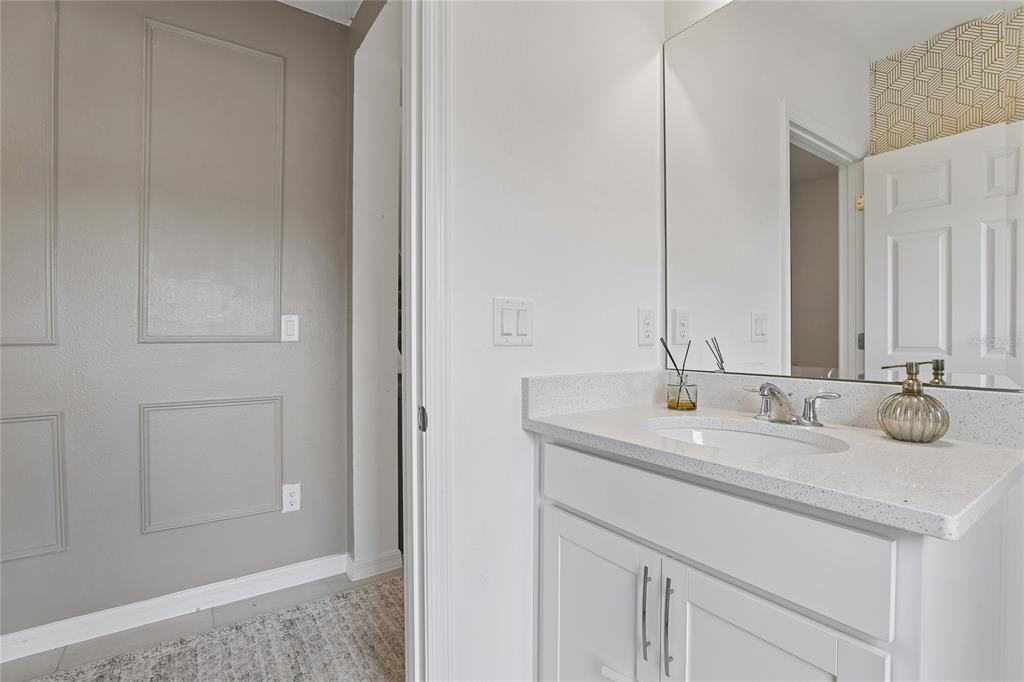 A bathroom features a white vanity with a quartz countertop, a mirror, and paneled walls — 1581 SWAN SWIM DRIVE, DAVENPORT, FL
