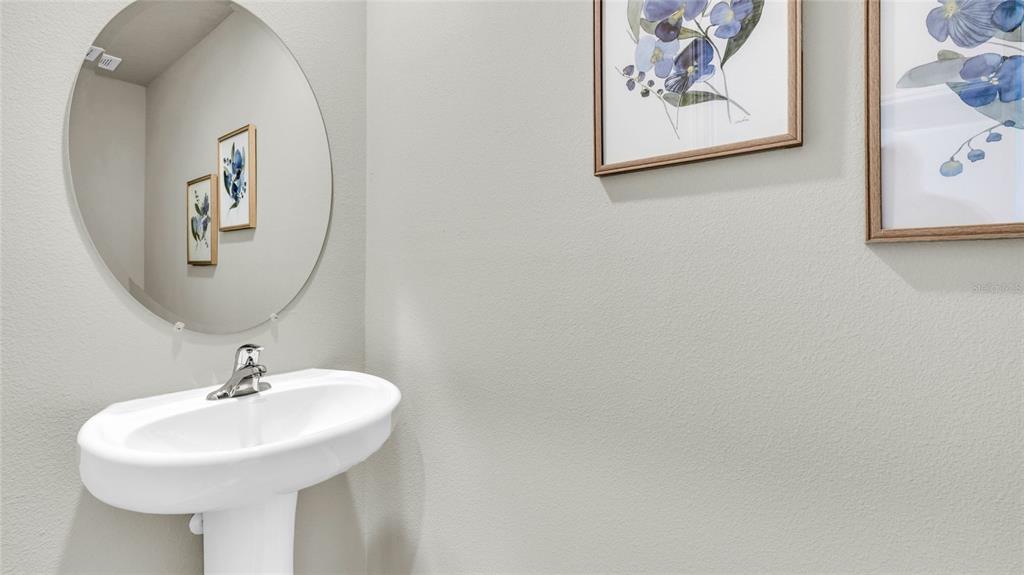A powder room features a white pedestal sink, a round mirror, and framed floral artwork — 4084 GOLD DUST LANE, SARASOTA, FL