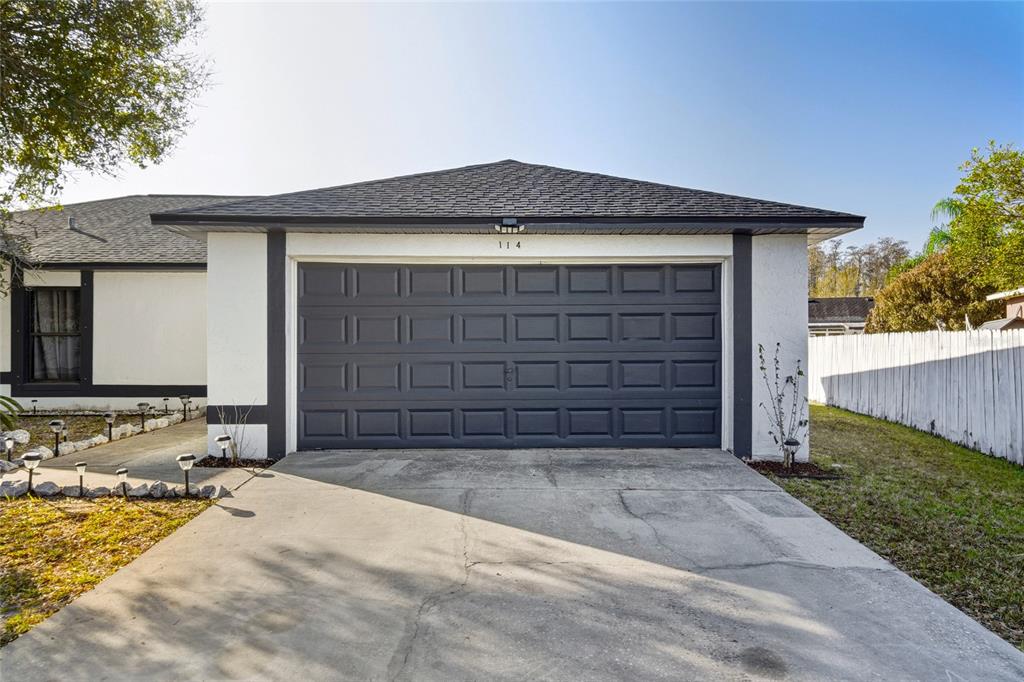 A dark gray garage door is centered on the front of a white stucco house — 114 DUNDEE LANE, KISSIMMEE, FL