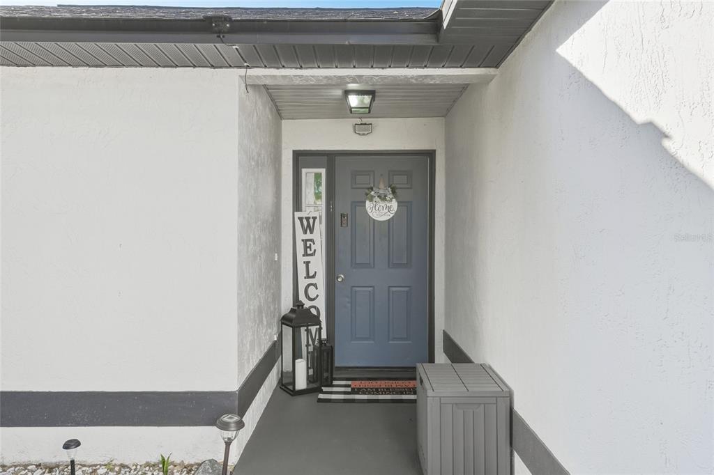 A covered entryway features a blue front door, a welcome sign, and a storage bin — 114 DUNDEE LANE, KISSIMMEE, FL