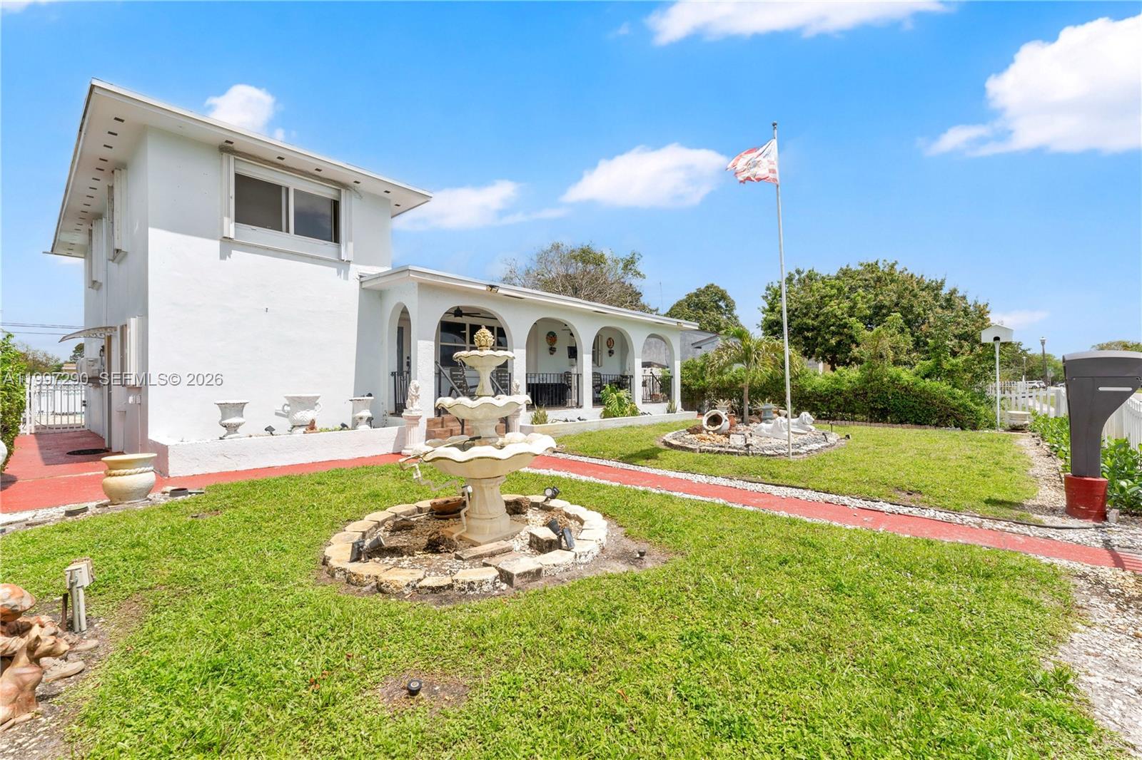A white two-story house features a front porch, a tiered fountain, and a flag pole — 1335 NW 129th St, North Miami FL 33167, NORTH MIAMI, FL