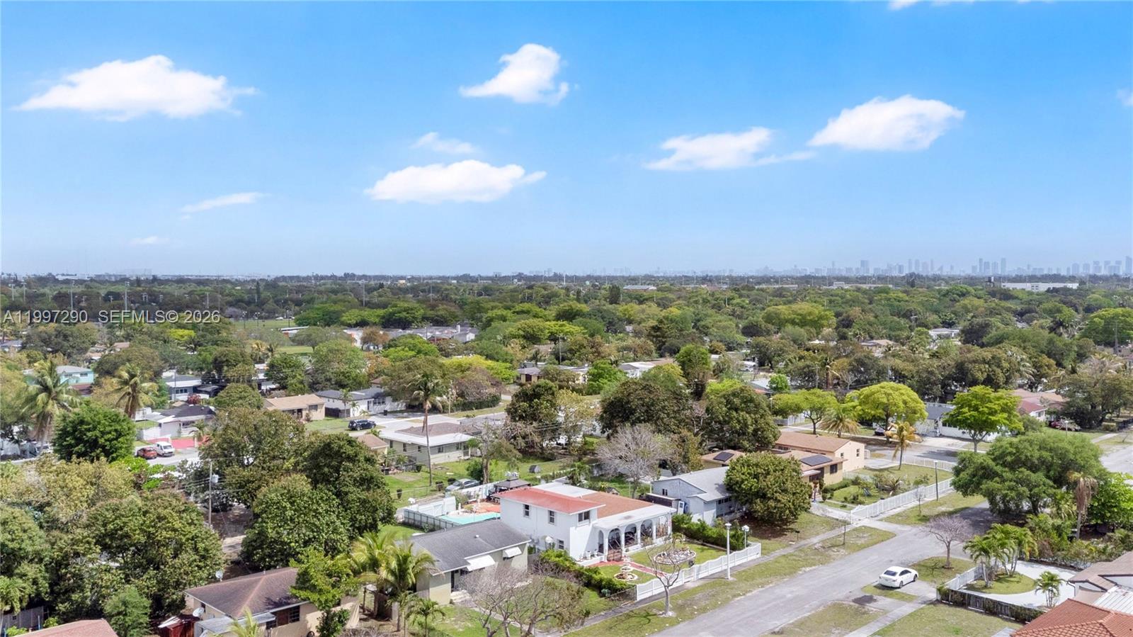 An aerial view shows a residential neighborhood with houses, lush trees, and a distant skyline — 1335 NW 129th St, North Miami FL 33167, NORTH MIAMI, FL